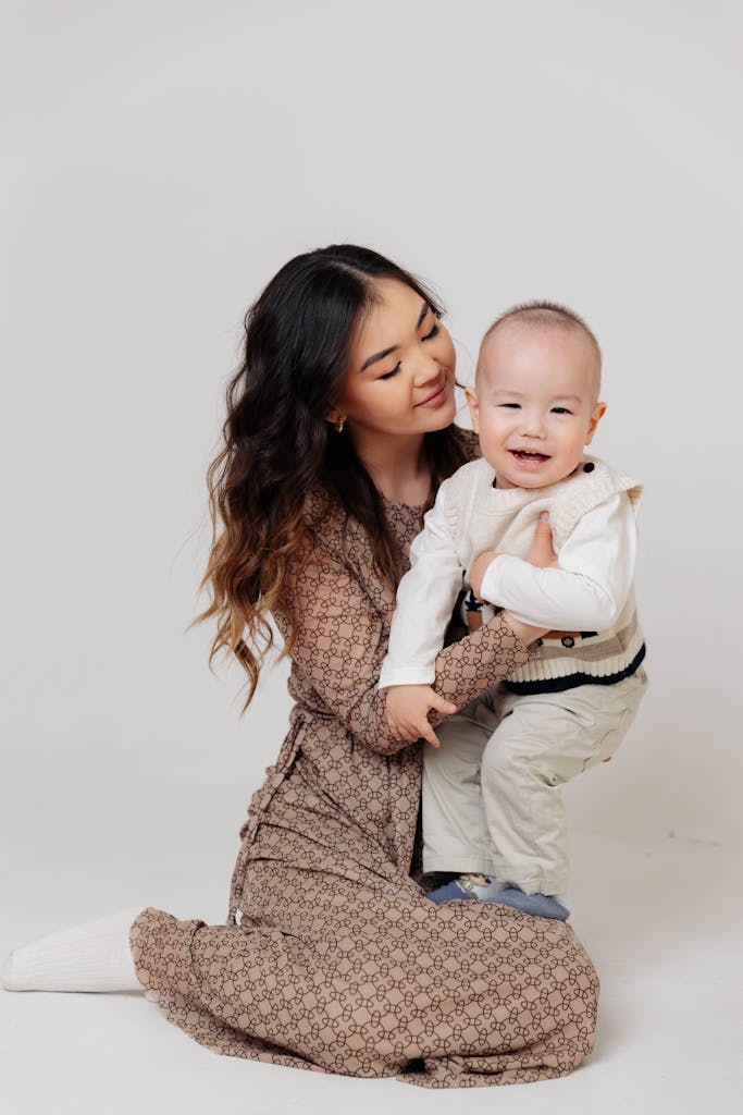 A loving mother holds her smiling baby in a studio setting, exuding warmth and joy.