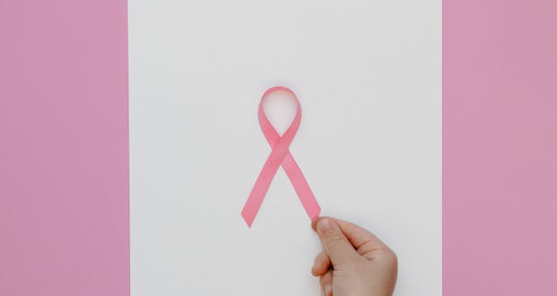 Pink ribbon for breast cancer awareness held by hand on a pink background.