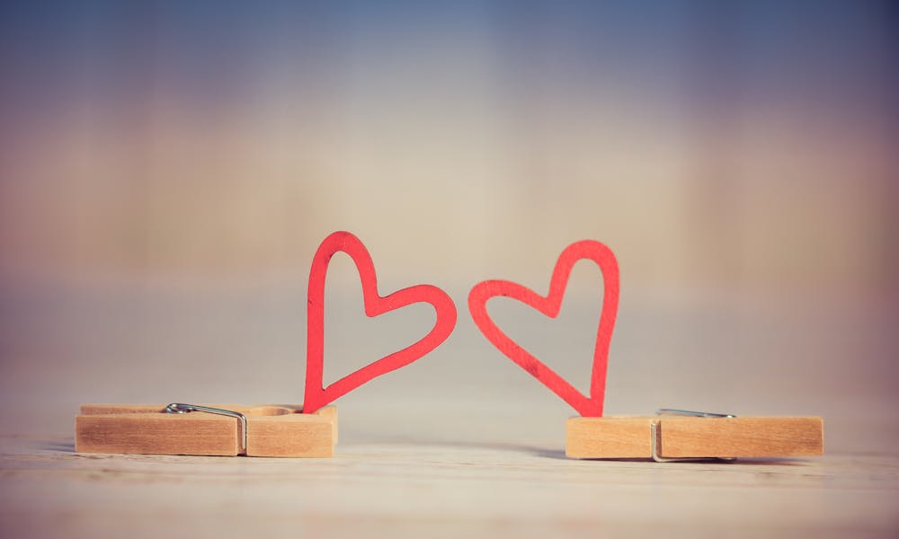 Two wooden clothespins with red heart shapes, symbolizing love and romance, on a blurred background.