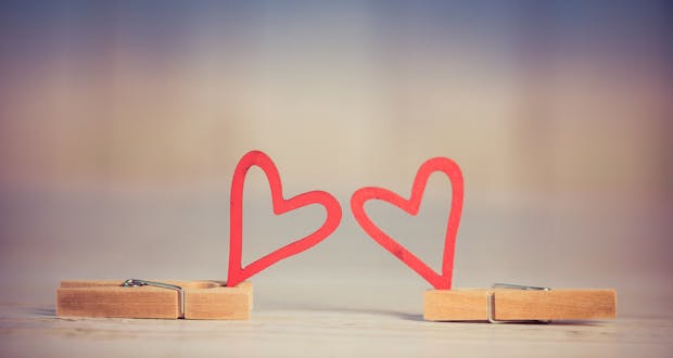 Two wooden clothespins with red heart shapes, symbolizing love and romance, on a blurred background.