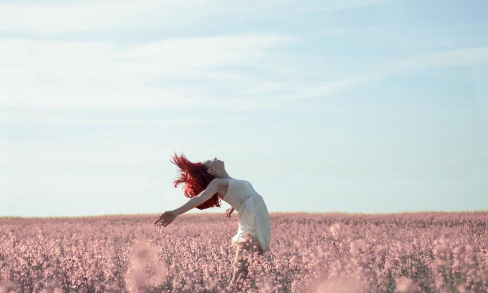 Woman with red hair in a white dress expressing freedom in a vibrant summer field.