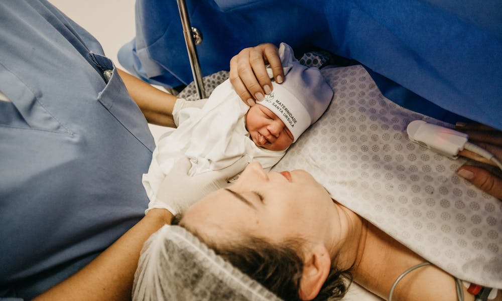 A mother cradling her newborn immediately after childbirth in a hospital setting.