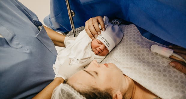 A mother cradling her newborn immediately after childbirth in a hospital setting.